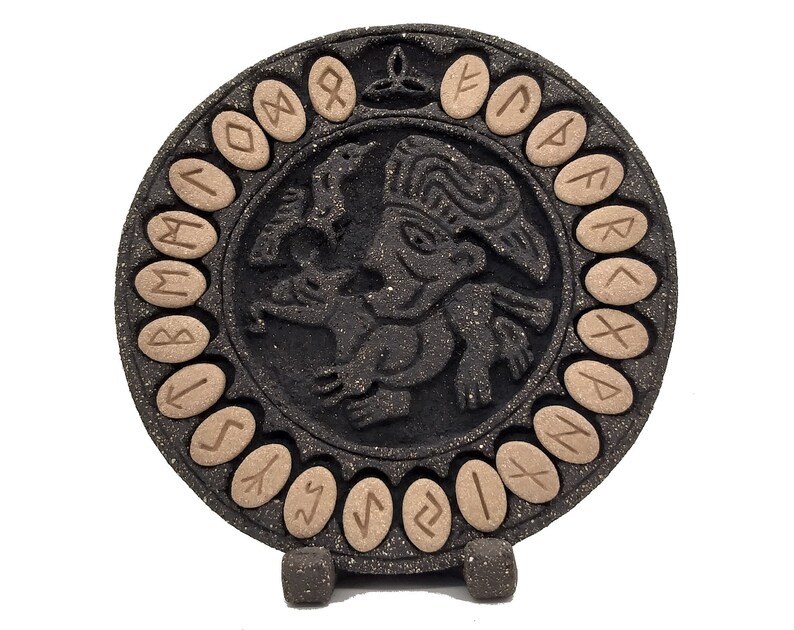 Plato circular de cerámica negra con figura mitológica en relieve y runas